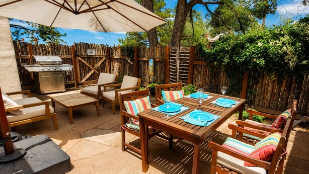 An outdoor patio with a wooden table set for four, surrounded by wooden chairs with colorful cushions. - The Birdhouse - Historic Adobe Architecture (Taos)