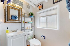 A bathroom with a white sink, a mirror with a decorative frame, a toilet, and a window. - The Birdhouse - Historic Adobe Architecture (Taos)