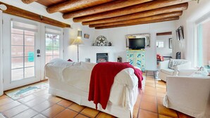 A living room with a white sofa, a red throw blanket, a television, and a fireplace. - The Birdhouse - Historic Adobe Architecture (Taos)