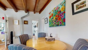 A dining area with a round wooden table, striped chairs, a colorful floral painting, and a framed picture on the wall. - The Birdhouse - Historic Adobe Architecture (Taos)