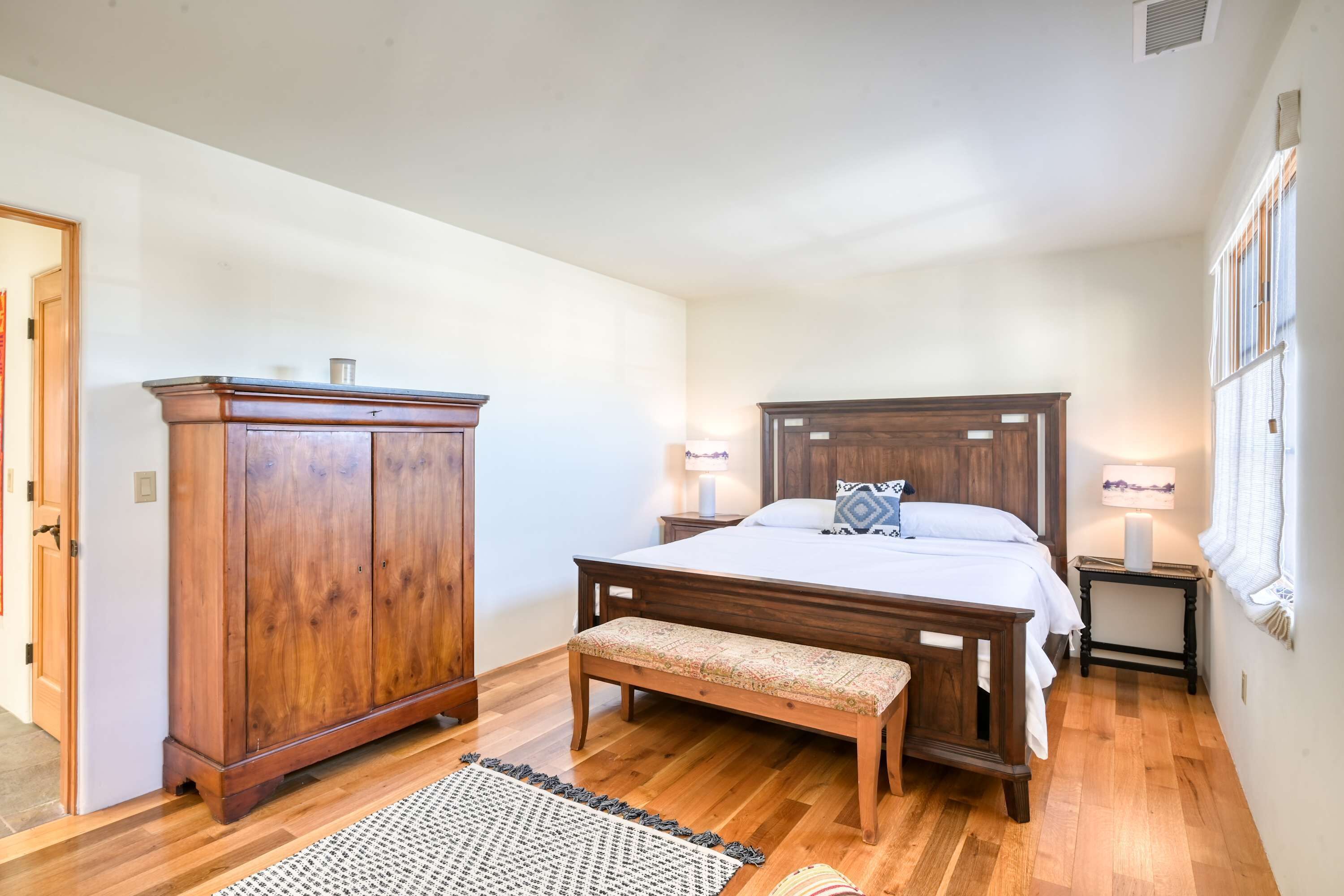 A bedroom with a wooden bed, a bench, a wardrobe, and a nightstand with lamps.