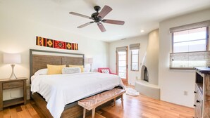 Ein Schlafzimmer mit einem Bett, Holzboden, Deckenventilator, Wandbildern, Nachttischlampen und einem Fenster.