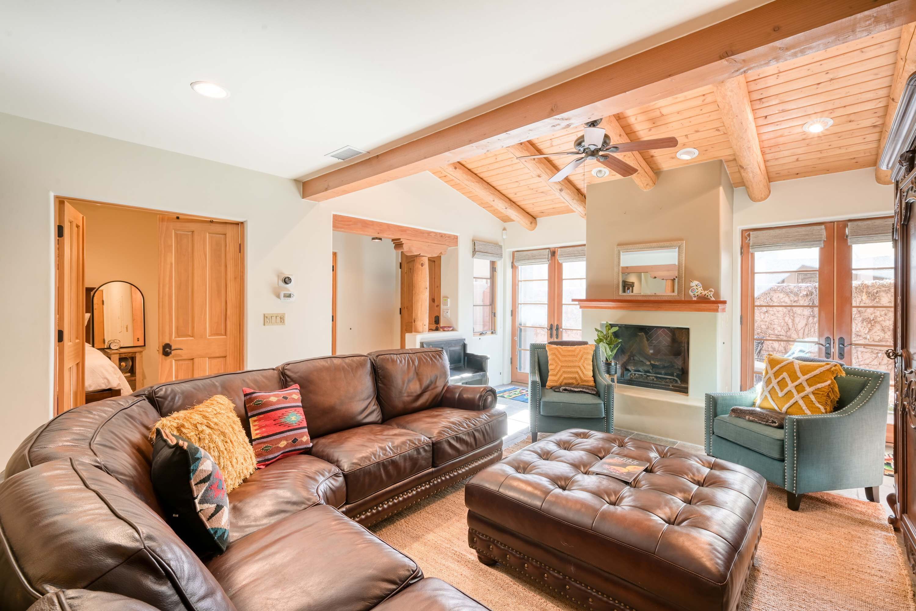 A spacious living room with a large leather sectional sofa, a tufted ottoman, and a blue armchair.