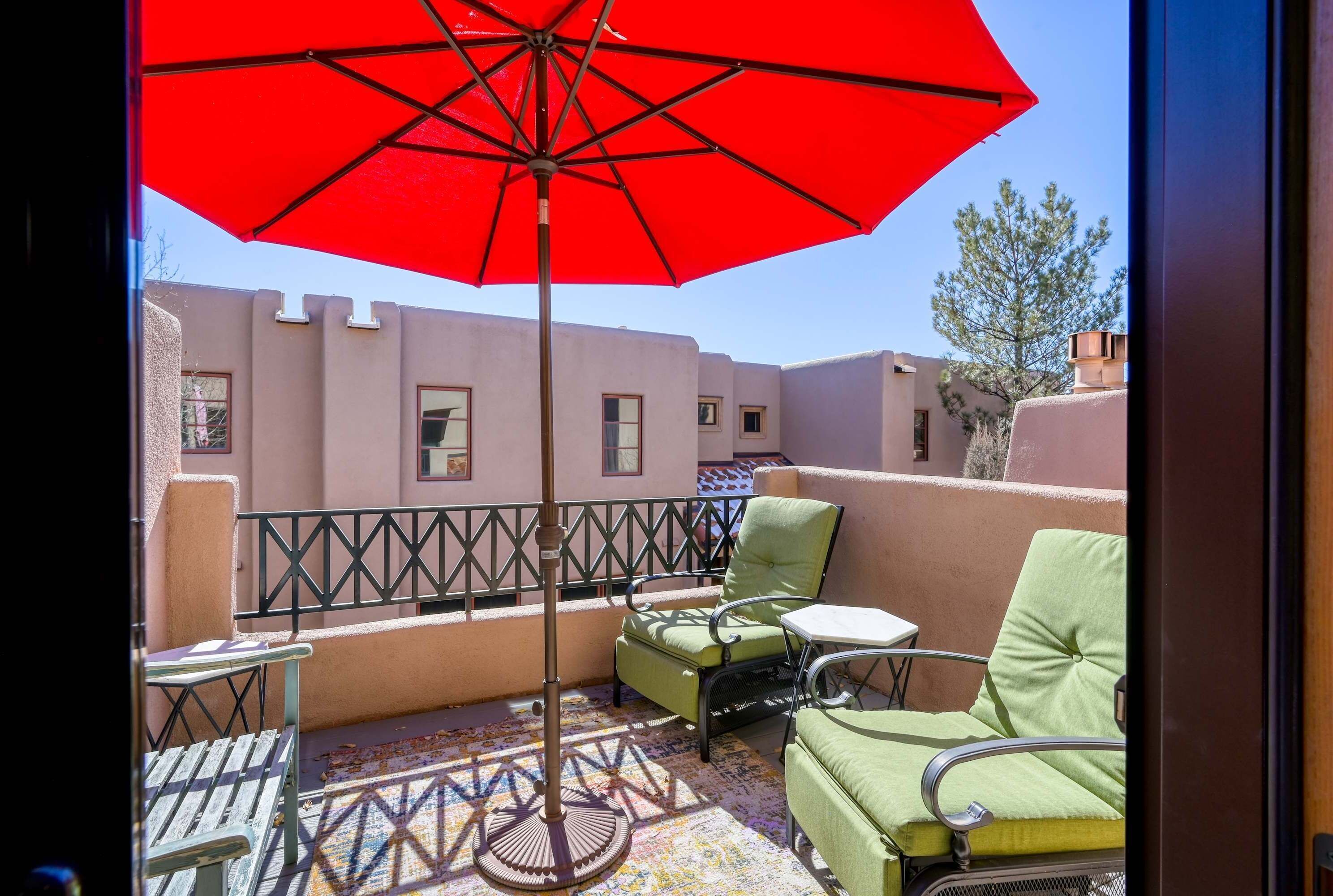 A balcony with a red umbrella, green chairs, a small table, and a patterned floor.
