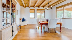 A dining area with a wooden table and chairs, a built-in cabinet, and large windows. - Dos Vistas - Firepit, Hot Tub, Mountain Views (Santa Fe)