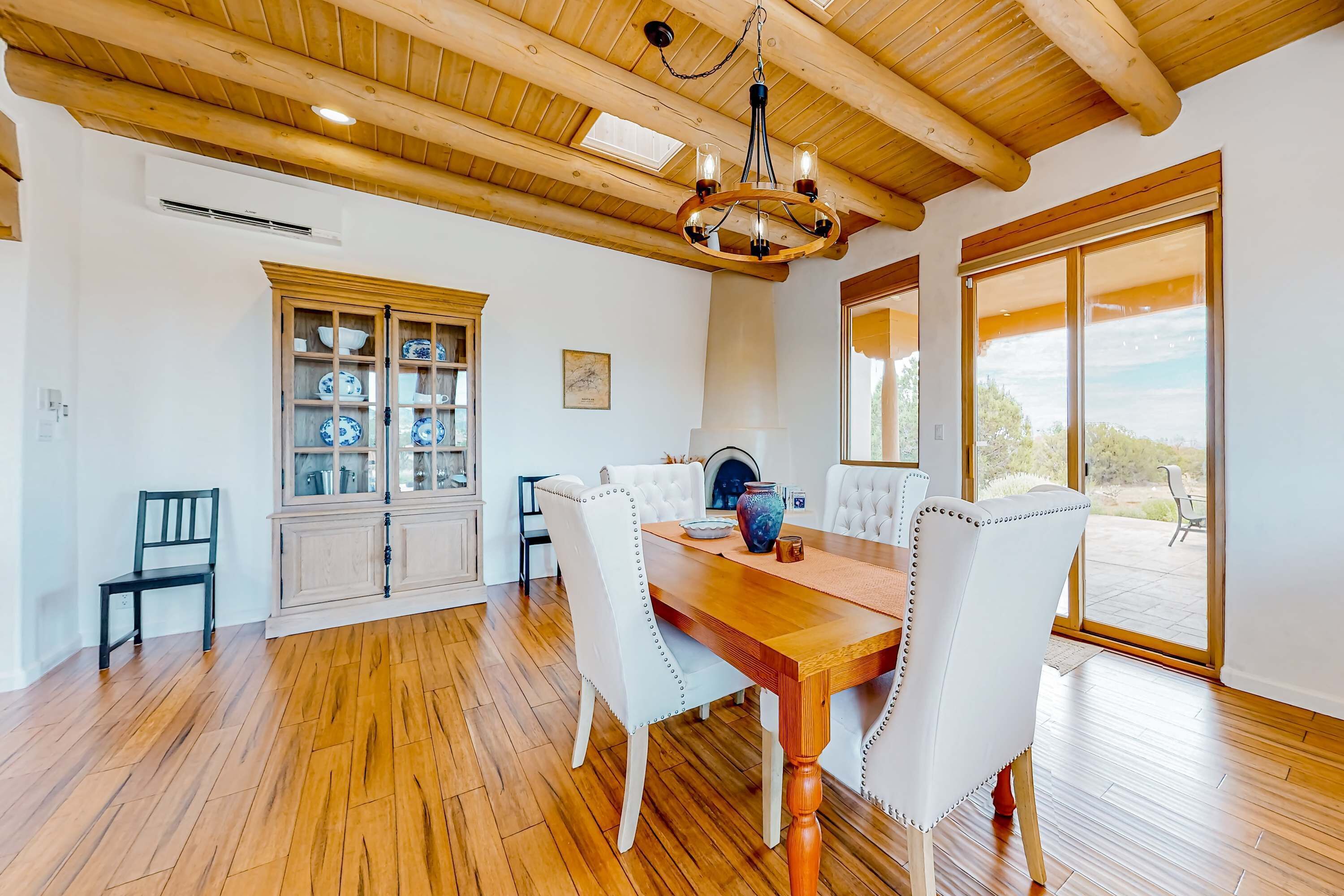 A dining area with a wooden table, white upholstered chairs, a chandelier, and a cabinet with dishes.