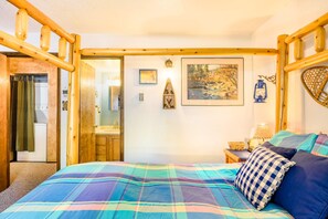 A bedroom with a plaid bedspread, wooden headboard, a nightstand with a lamp, and a framed picture on the wall. - Outdoor Hideout - Walk to Ski, Hike, Bike & Dining (Angel Fire)