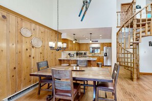 A wooden-paneled dining area with a central island, a kitchen with modern appliances, and a wooden staircase. - Snowfire 308A - Views & Walk or Shuttle to Lifts (Angel Fire)