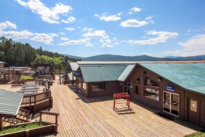 A wooden deck with outdoor seating, a rental entrance, and a building with a green roof. - Snowfire 308A - Views & Walk or Shuttle to Lifts (Angel Fire)