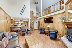 A spacious living area with a wooden floor, a fireplace, a dining area, and a staircase leading to an upper level. - Snowfire 308A - Views & Walk or Shuttle to Lifts (Angel Fire)