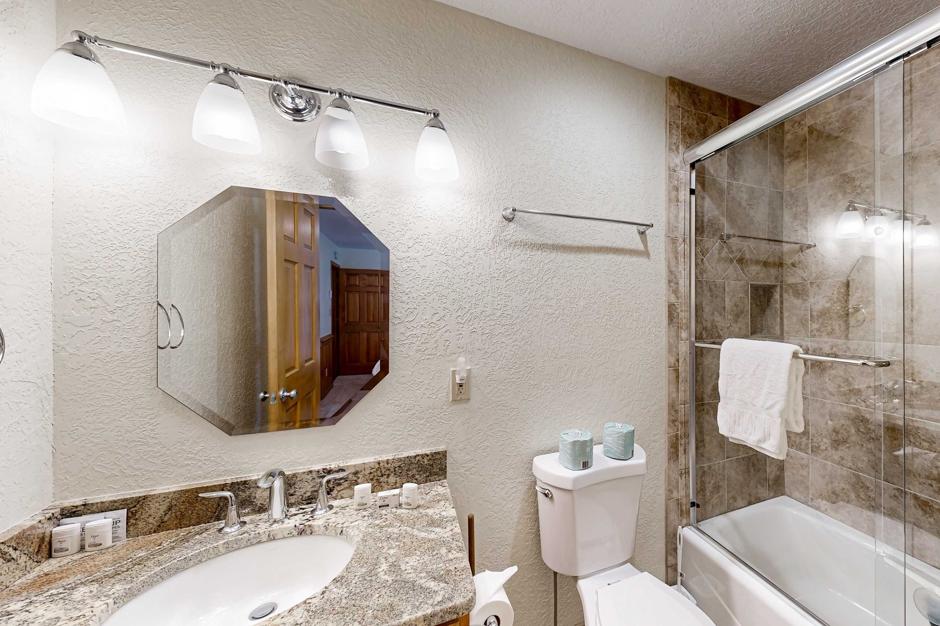 A bathroom with a granite countertop, a sink, a mirror, a toilet, and a glass-enclosed shower.