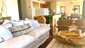 Een woonkamer met een bank, stoelen, een lamp en een eethoek met een tafel en stoelen.