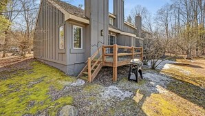Ein modernes Haus mit einer Holztreppe zu einer Terrasse, umgeben von Bäumen und einer Rasenfläche.