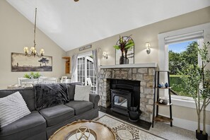 A living room with a stone fireplace, a sofa, a dining table, and a view of the outdoors. - Mystic Lodge • Ski Jack Frost + Lake Club Access (Lake Harmony)