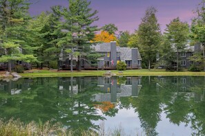 Un chalet au bord du lac, doté de plusieurs cabanes, d’une terrasse en bois et dont l’image se reflète dans l’eau.
