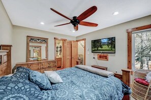 Een slaapkamer met een bed, een houten dressoir, een plafondventilator, een televisie en een raam met uitzicht.