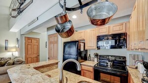 Eine Küche mit Granit-Arbeitsplatten, einer Edelstahl-Spüle, einem schwarzen Kühlschrank, einem Herd und Holzschränken.