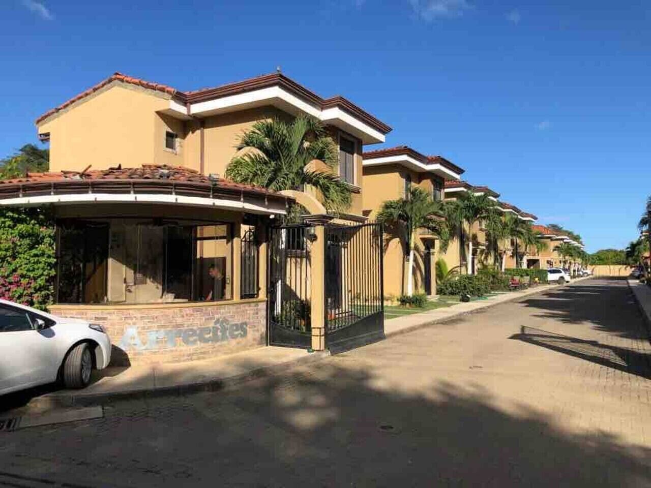 A residential street with houses, a gated entrance, and a parked car.
