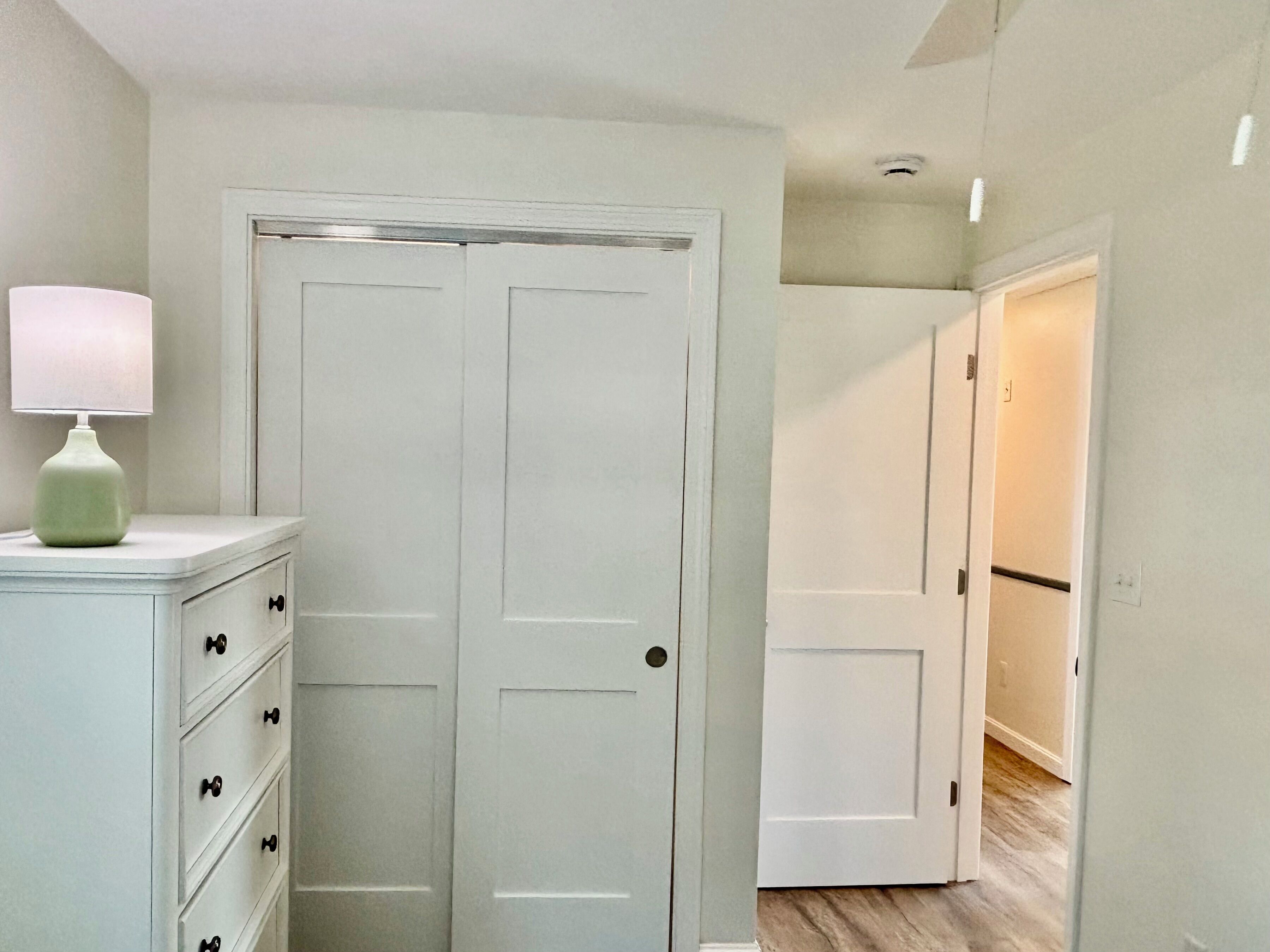 A hallway with a white door, a dresser with drawers, and a lamp.