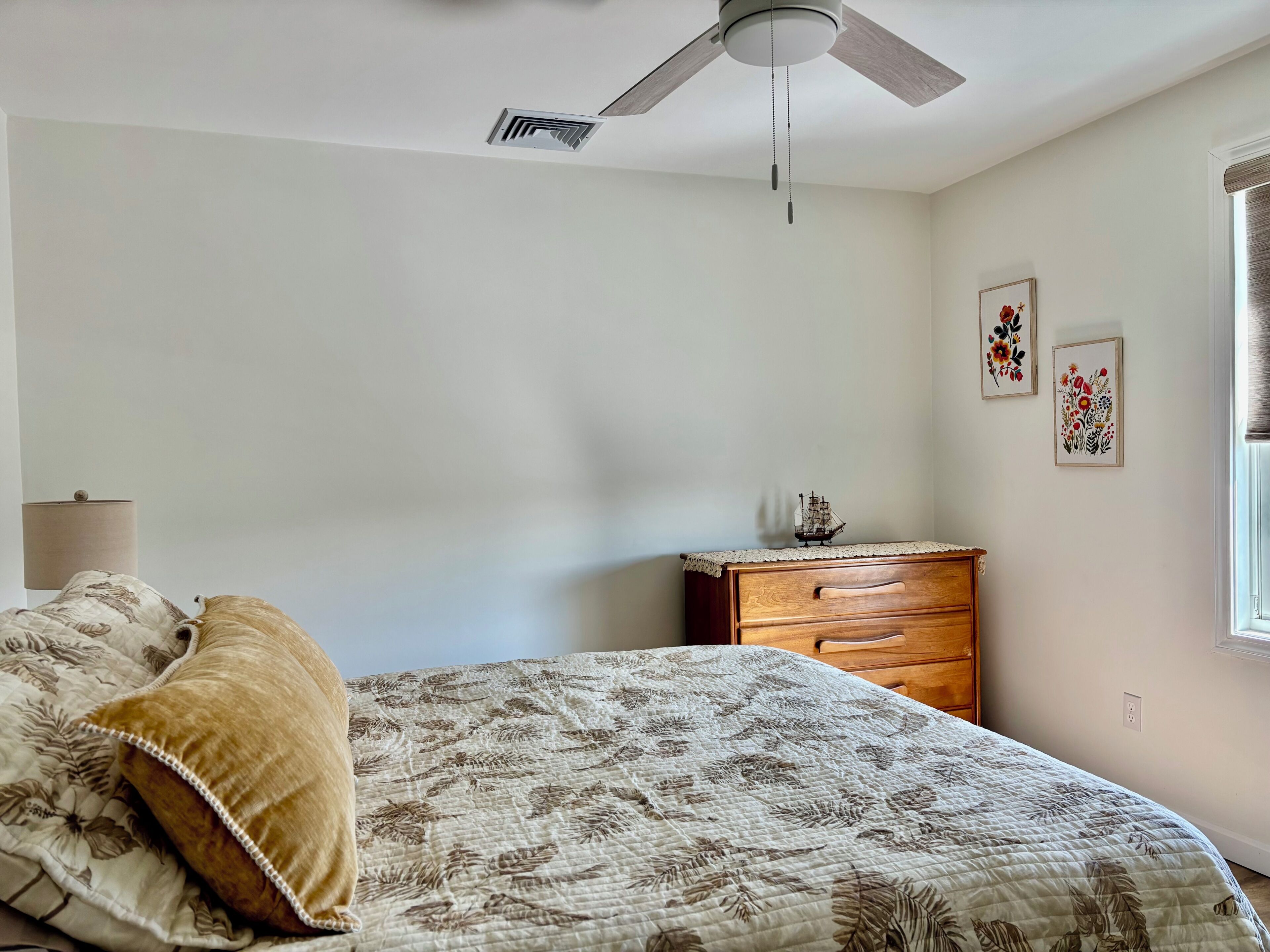 A bedroom with a bed, a dresser, a ceiling fan, and wall art.