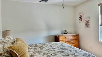 A bedroom with a bed, a dresser, a ceiling fan, and wall art.