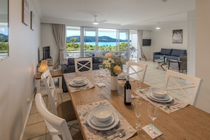 A dining area with a table set for four, a sofa, and a view of the outdoors. - Poinciana 104 & Free Buggy - Hamilton Island (Hamilton Island)