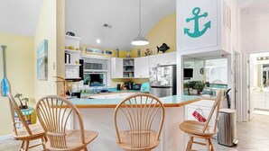 A kitchen with a central island, wooden chairs, and a large anchor decoration on the wall. - Spacious ocean front house with spectacular views in Nags Head with Elevator (Nags Head)