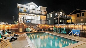 A pool area with lounge chairs, a staircase leading to a second floor, and a building with multiple balconies. - Spacious ocean front house with spectacular views in Nags Head with Elevator (Nags Head)