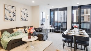 A modern living room with a sofa, coffee table, and dining area with chairs and a table set for four. - 3 Bedroom CBD Apartment with Pool, Gym & Spa with Gorgeous City Views (Melbourne)