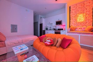 A modern living room with a sofa, a glass coffee table, and a kitchen in the background.