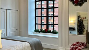 A bedroom with a bed, a window with a view of buildings, a chandelier, and a wreath on the wall. - Luxury Downtown Indy • Walk to NCAA Final Four • On American Legion Mall (Indianapolis)