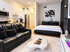 A modern apartment with a kitchen, a living area with a black leather sofa, a white coffee table, and a bed with a black headboard. - Cozy Theater Studio Houston 10 min from downtown (Houston)