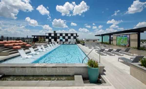 Área de piscina no terraço com espreguiçadeiras e um edifício quadriculado ao fundo.