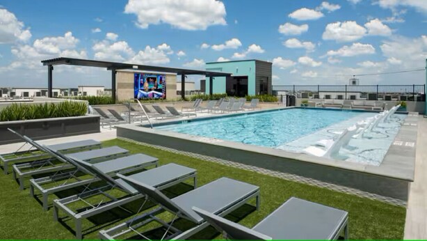Ein Pool auf dem Dach mit Liegestühlen, einer überdachten Sitzgelegenheit und einem Gebäude mit Wandgemälde.