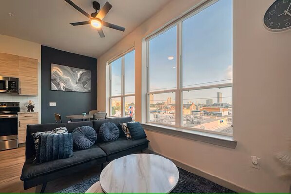 A modern living room with a sofa, coffee table, and a city view through large windows. - Peaceful Heights One-Bed - Views & Comfort (Houston)