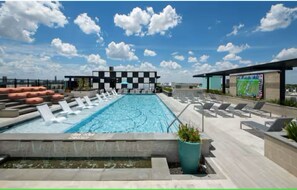 A rooftop pool with a checkered wall, lounge chairs, and a large screen. - Peaceful Heights One-Bed - Views & Comfort (Houston)