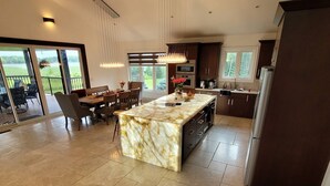 A spacious kitchen with a marble island, dark cabinetry, and a large window overlooking a green landscape. - Devlok- Mystique Mansion 7 Br-sleep 16 Kawartha (Trent Lakes)