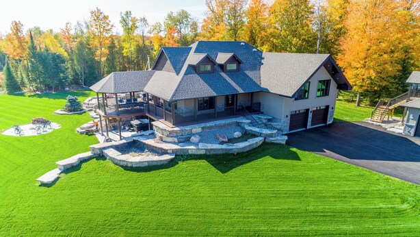 A large, modern house with a spacious deck, a stone fire pit, and a well-maintained lawn. - Devlok- Mystique Mansion 7 Br-sleep 16 Kawartha (Trent Lakes)
