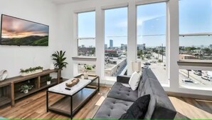 Ein modernes Wohnzimmer mit großem Fenster, einer Couch, einem Couchtisch und einem Fernseher.