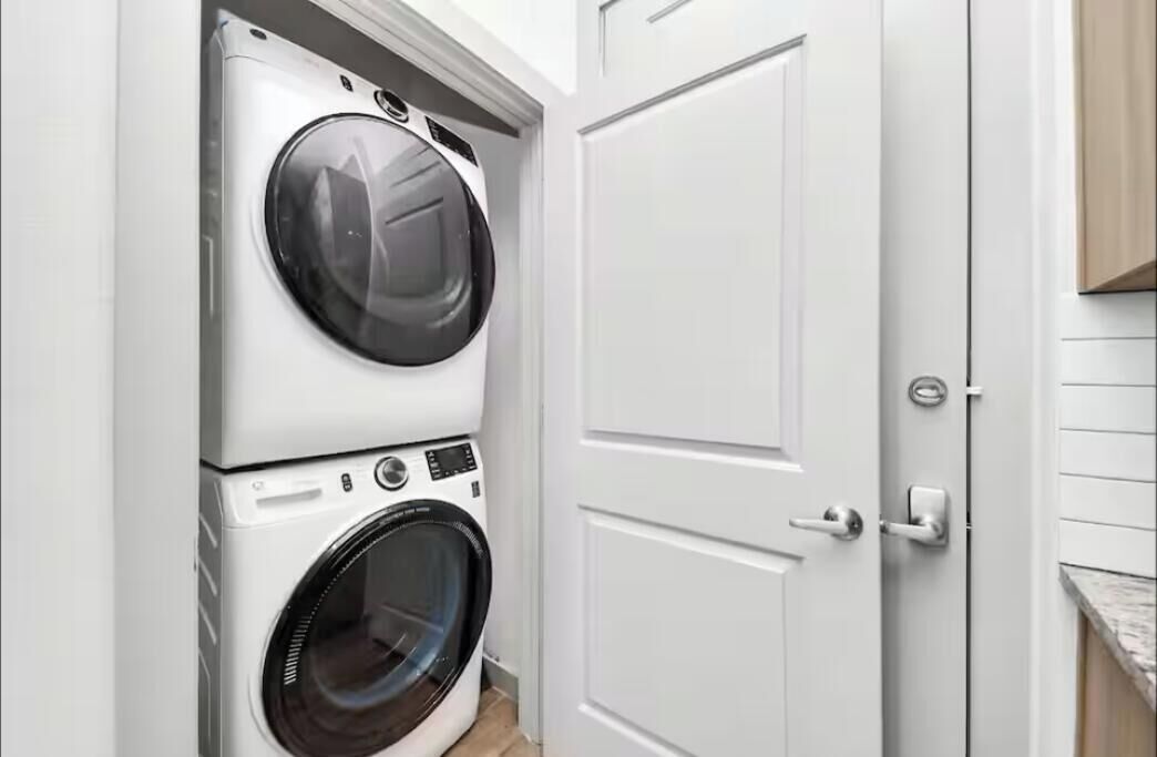 A laundry room with stacked washers and dryers, a white door, and a wooden cabinet.