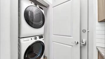 A laundry room with stacked washers and dryers, a white door, and a wooden cabinet.