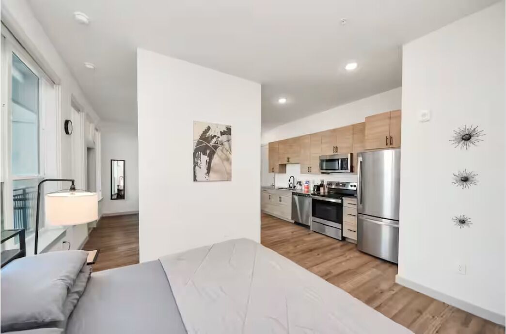 A modern apartment with a bed, a kitchen with stainless steel appliances, and a minimalist decor.