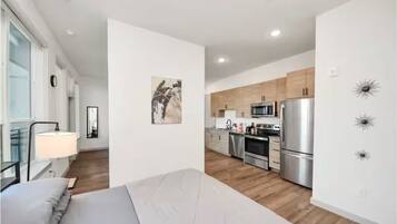 A modern apartment with a bed, a kitchen with stainless steel appliances, and a minimalist decor.