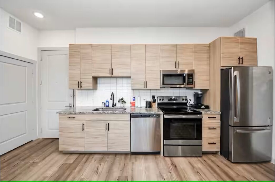 A modern kitchen with light wood cabinets, stainless steel appliances, and a tiled backsplash.