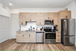 A modern kitchen with light wood cabinets, stainless steel appliances, and a tiled backsplash. - Luxury Gold Heights 1BR w- Skyline Views (Houston)