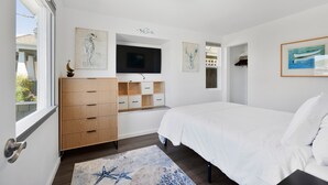 Une chambre à coucher comprenant un lit, un téléviseur fixé au mur, une armoire en bois et des œuvres d’art.