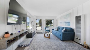 Un salon moderne avec un canapé bleu, une table basse, un téléviseur fixé au mur et une grande fenêtre.