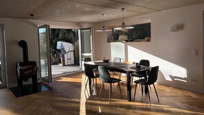 A modern dining area with a wooden floor, a table with chairs, and a large window allowing natural light. - Vacation home for 8 people with natural garden, fireplace & lots of space, near the North Sea (Wesselburen)