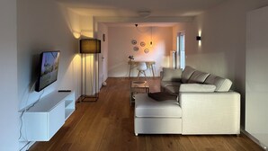A modern living room with a flat-screen TV, a floor lamp, a sofa, and a coffee table. - Vacation home for 8 people with natural garden, fireplace & lots of space, near the North Sea (Wesselburen)