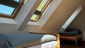 A room with a sloped ceiling, skylights, a wooden bed, and a herringbone-patterned floor. - Vacation home for 8 people with natural garden, fireplace & lots of space, near the North Sea (Wesselburen)